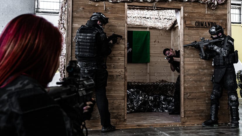 Giocatori in tenuta nera attorno all'ingresso di una casetta di legno nell'arena di Softair Milano